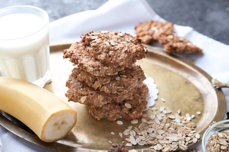 banana and oat cookies on a tray with a glass of milk behind