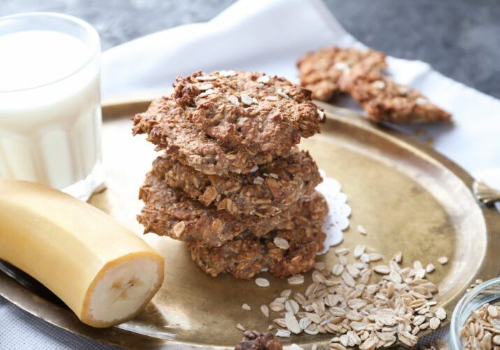 banana and oat cookies on a tray with a glass of milk behind