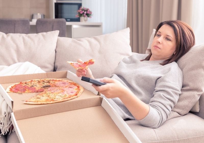 woman eating pizza on sofa, the relationship between food and mood | Perpetual Wellbeing