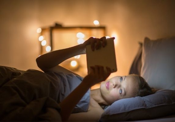 woman using device in bed | why is melatonin important for sleep | Perpetual Wellbeing